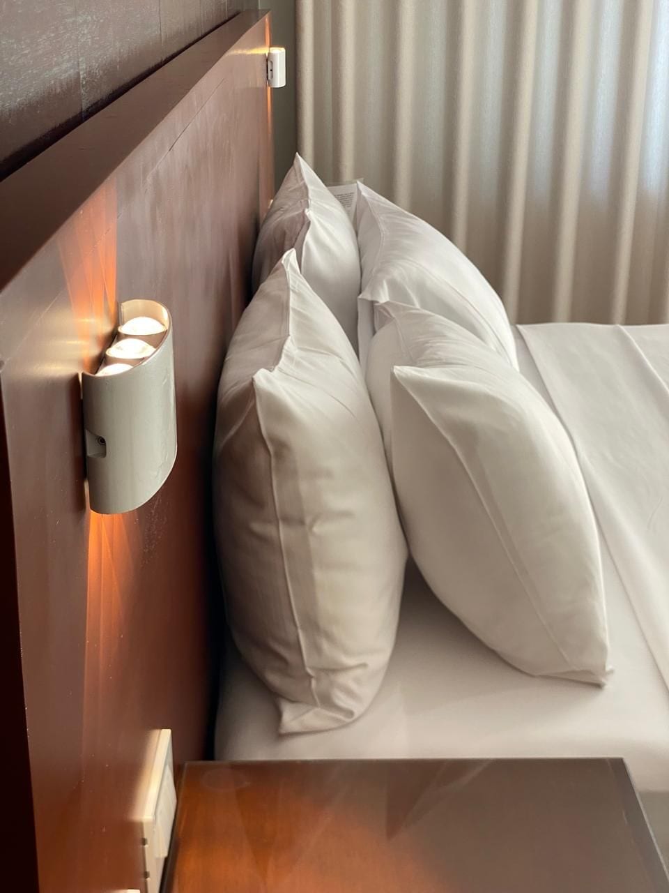 A hotel room with a wooden headboard, a bedside table, and two white pillows.