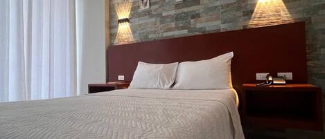 A modern hotel room with a large bed, two bedside tables with lamps, a stone-patterned wall, and a window with curtains.