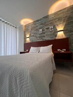 Habitación de hotel moderna con una cama grande, dos mesitas de noche con lámparas, una pared con diseño de piedra y una ventana con cortinas.