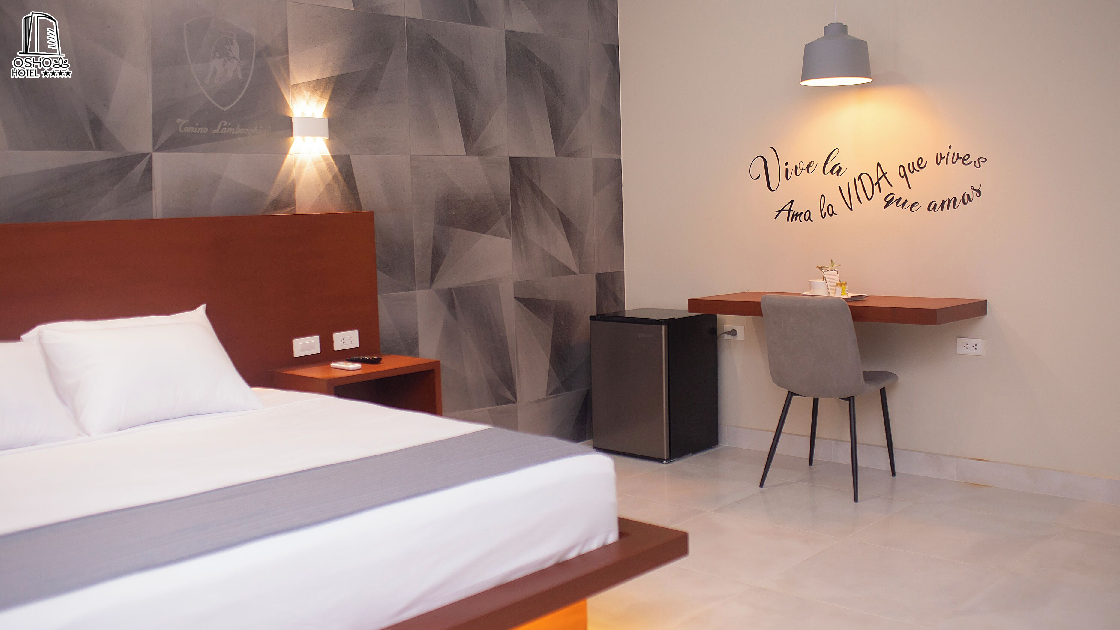 A hotel room with a bed, a desk, a chair, a small refrigerator, and a wall with a motivational quote.