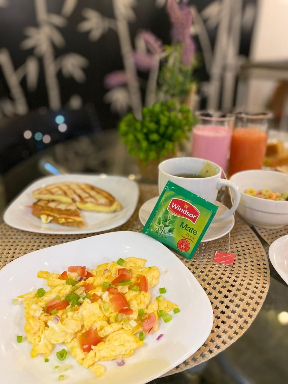 Una mesa de desayuno con platos de huevos revueltos, tostadas y una bolsita de té Windsor Mate.