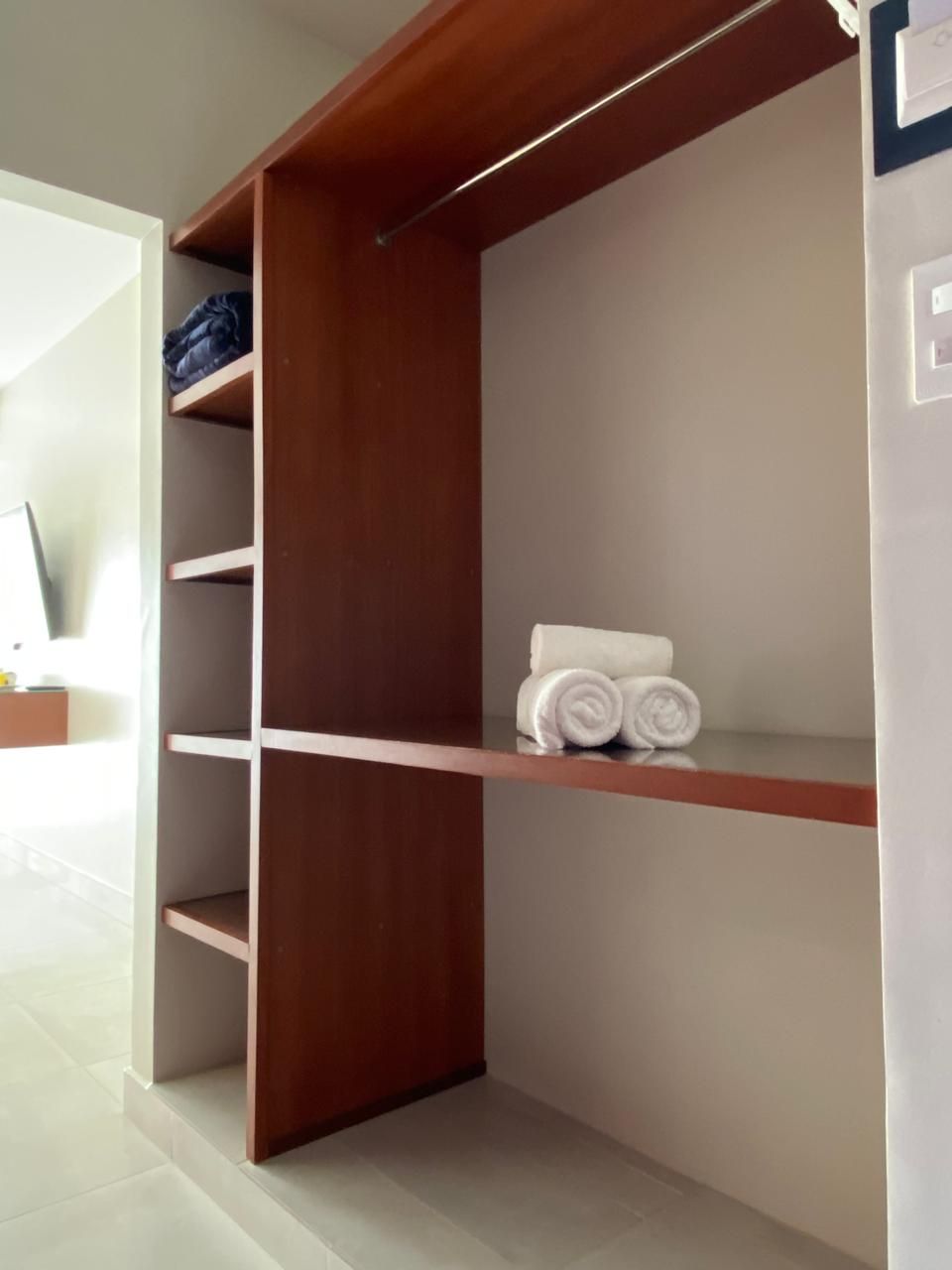 A wooden closet with shelves and a hanging rod, a white towel on the top shelf, and a door leading to another room.