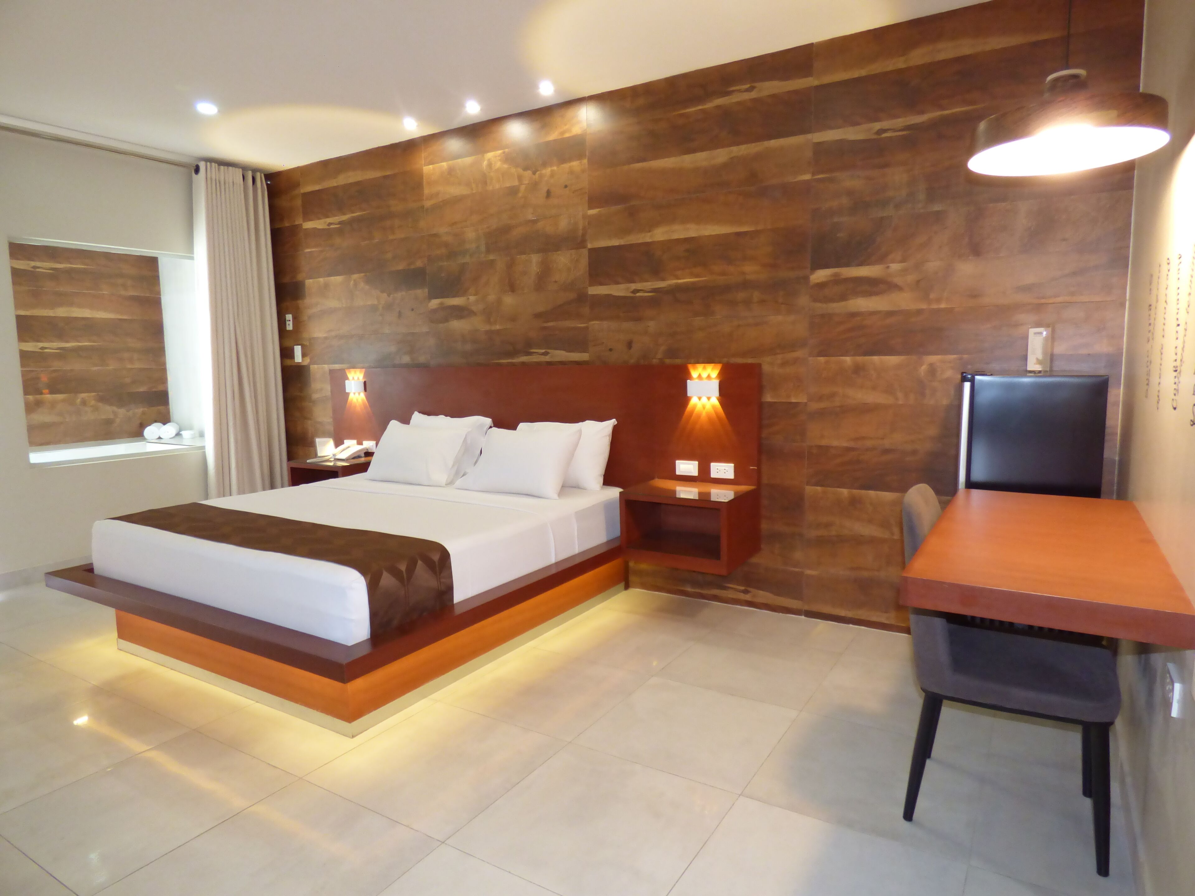 A modern hotel room with a large bed, bedside tables, a desk, and a chair.