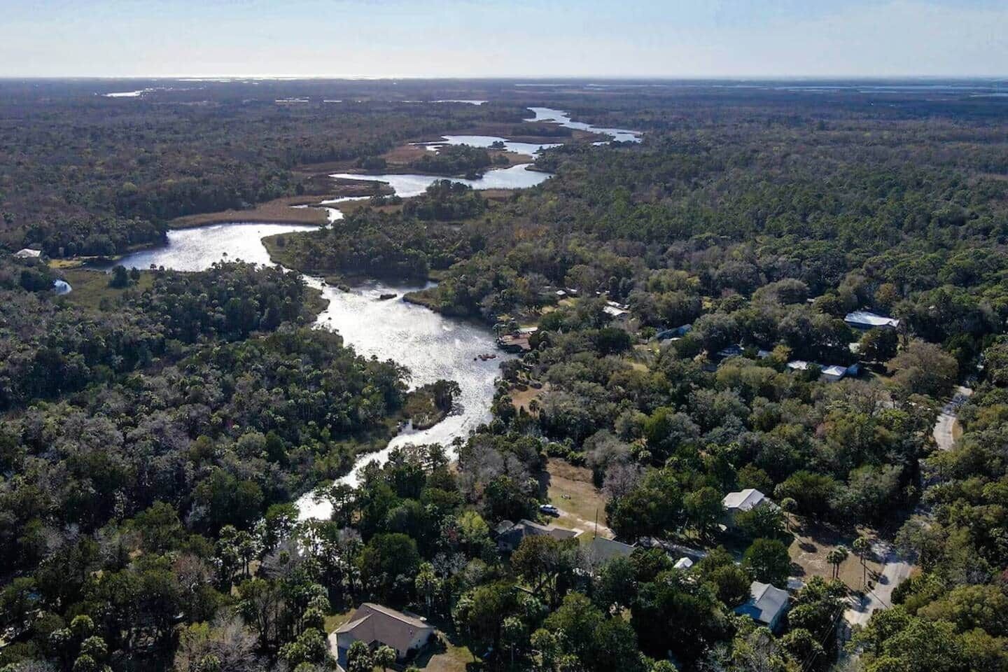 An aerial view of a river winding through a densely forested area with scattered buildings.