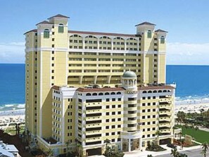 A multi-story hotel with a central dome and a beach view.