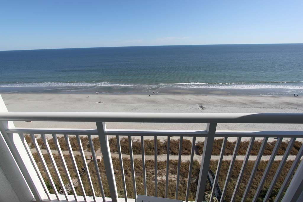 Blick auf einen Strand vom Balkon mit Geländer, feiner Sand und Meer.