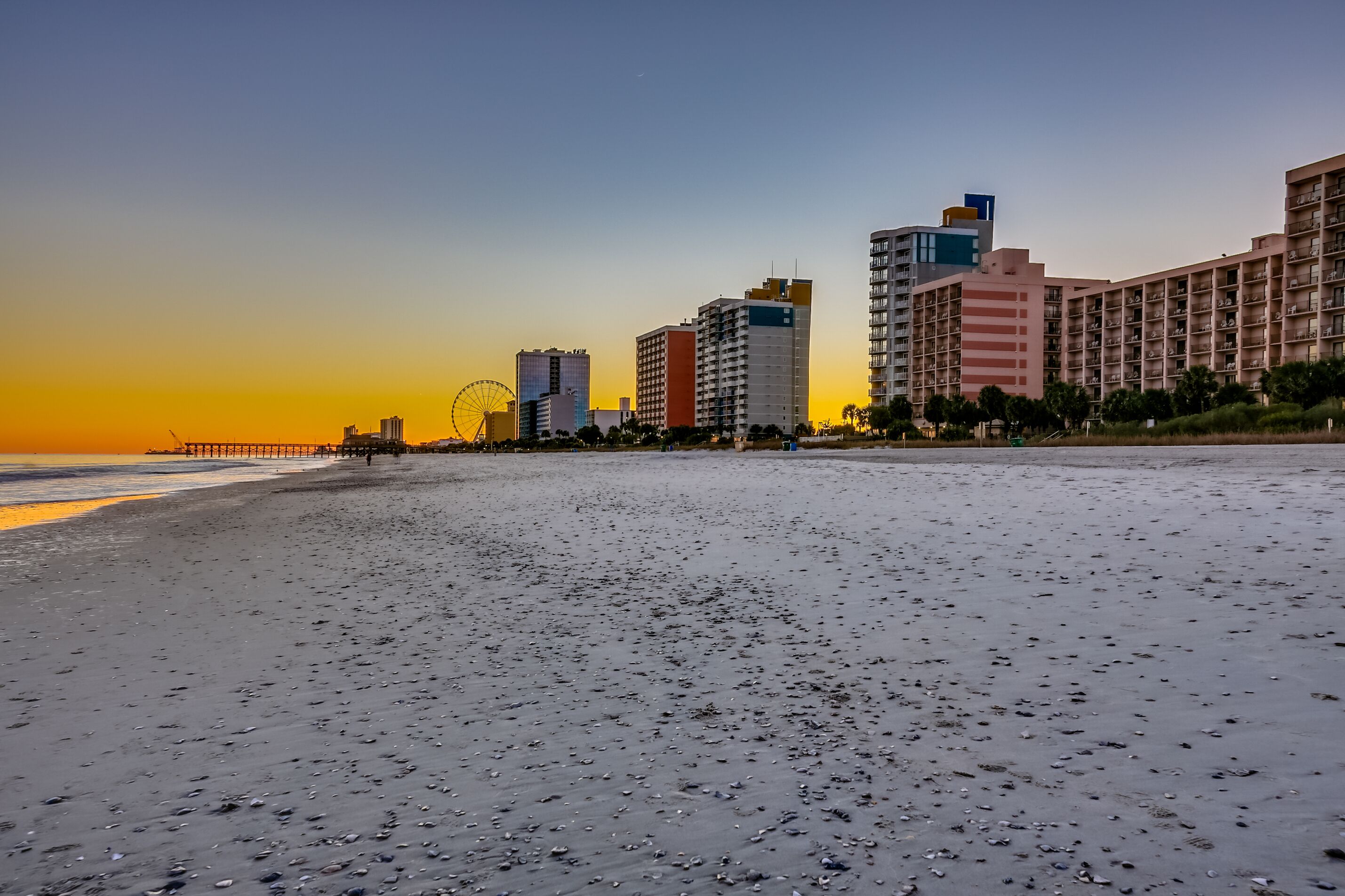 A beach with a pier extending into the water, surrounded by high-rise buildings.