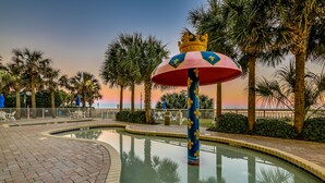 A pool area with a decorative fountain, palm trees, and a sunset in the background. - Spectacular Beach Condo Double Suite for 2 couples (Myrtle Beach)