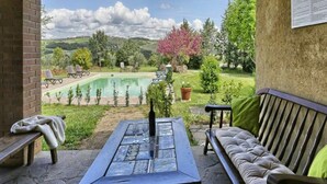 Alpendre coberto com mesa de pedra, um banco estofado e vista para uma piscina e jardim.
