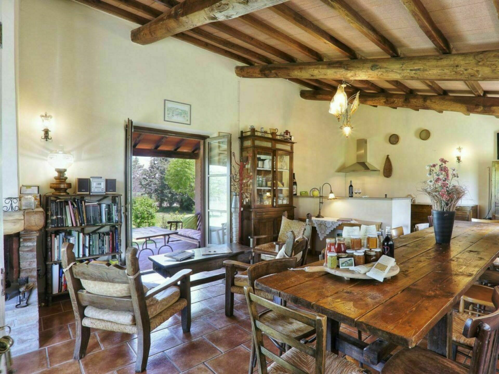 A rustic dining area with a wooden table and chairs, a bookshelf, and a view of the outdoors.