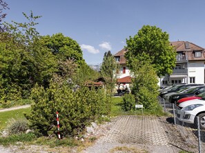 Een woonwijk met een verharde oprit die leidt naar een huis met een rood dak, omringd door groen en geparkeerde auto's.