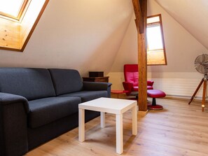Um quarto estilo loft com um sofá cinza escuro, uma mesa branca, uma cadeira vermelha e piso de madeira.