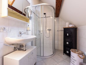 A modern bathroom with a glass-enclosed shower, a white sink, and a black storage unit with numbered compartments.