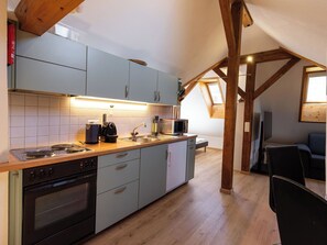 A compact kitchen with modern appliances, a dining area with a table and chairs, and a sloped ceiling with wooden beams.