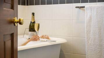 A bathtub with a bottle of champagne and a glass.