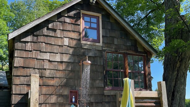 Eine rustikale Holzhütte mit kleinem Fenster, einer Holzleiter und einer weißen Badewanne.