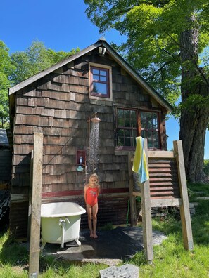 A rustic wooden cabin with a small window, a wooden ladder, and a white bathtub.
