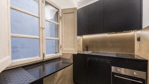 Une cuisine compacte dotée d’une fenêtre, de meubles noirs, d’un évier en acier inoxydable et d’un four encastré.