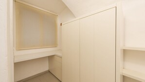 Une petite pièce fermée, avec une fenêtre, une armoire blanche et un sol carrelé.