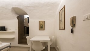Une pièce avec une table blanche, quatre chaises, un lit, un téléviseur et un téléphone fixé au mur.