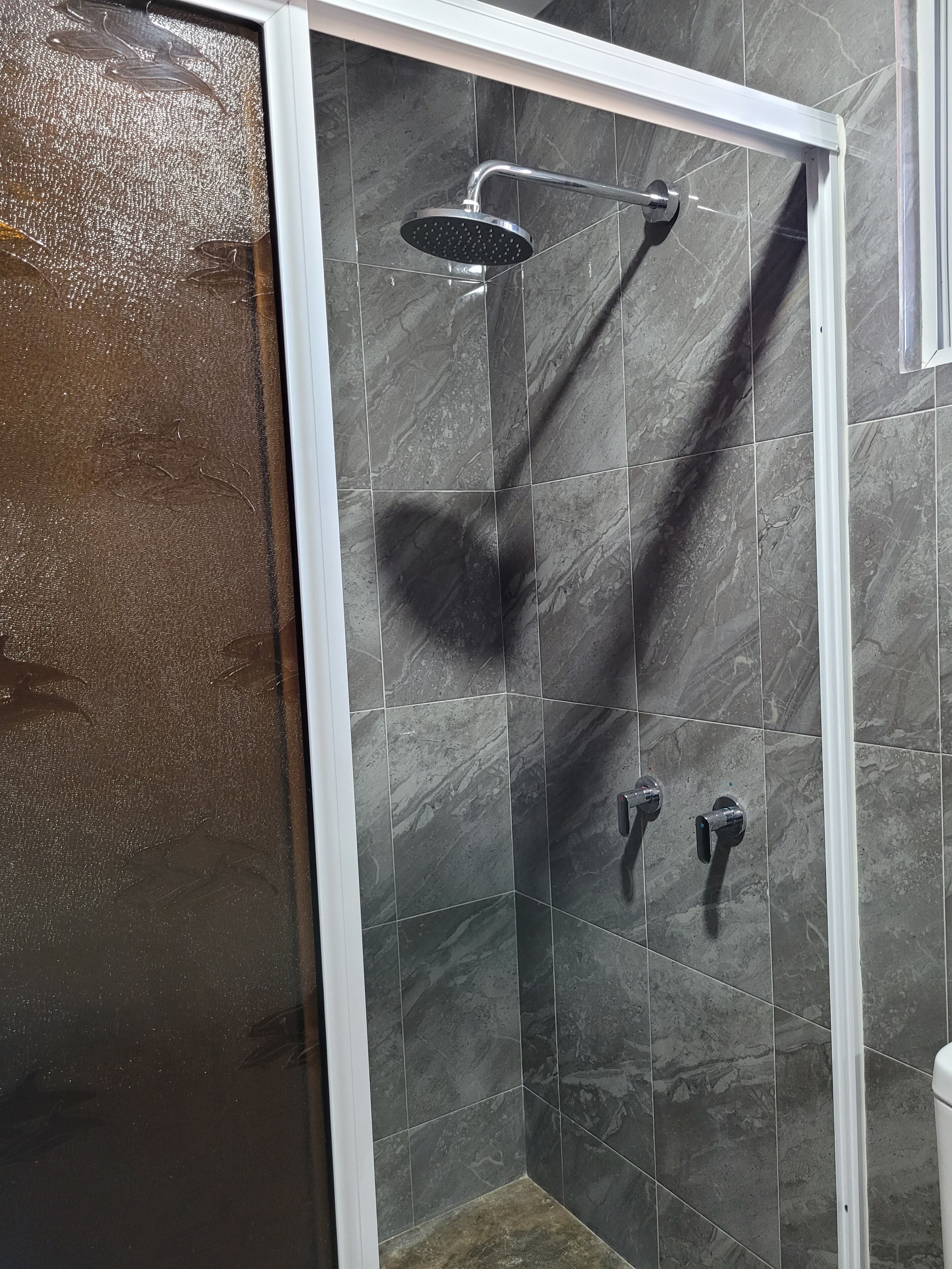 A shower area with a glass door, dark tiled walls, and a metal showerhead.