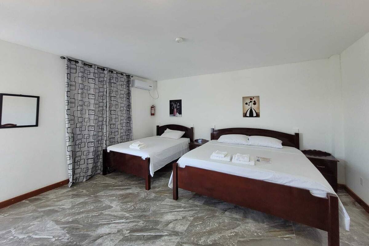 A hotel room with two single beds, a stone-patterned floor, a window with patterned curtains, and a ceiling light.