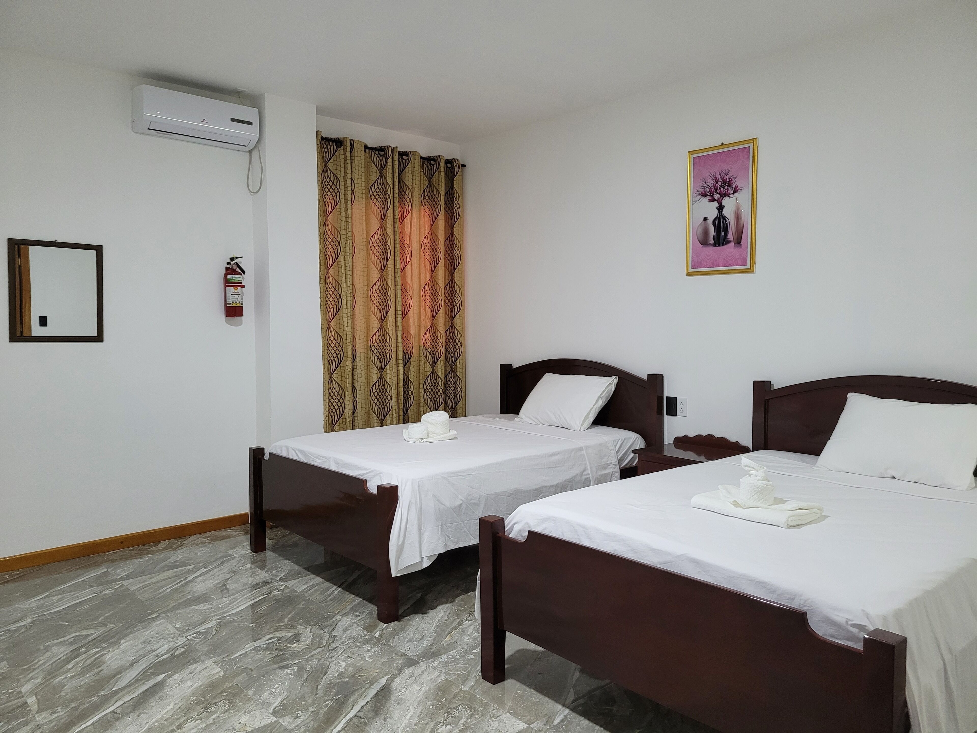 Ein Hotelzimmer mit zwei Betten, einem Feuerlöscher, einer Klimaanlage und einem gerahmten Bild an der Wand.