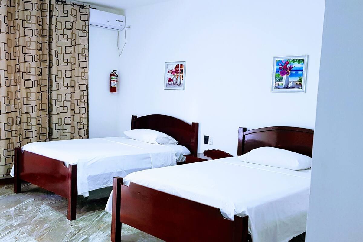 A room with two single beds, a patterned curtain, a fire extinguisher, and wall art.