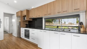 A modern kitchen with wooden cabinets, a black countertop, and a large window offering a view of the outdoors. - Top of the Bay by Ready Set Stay (Arthurs Seat)
