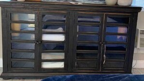 A bedroom with a dark wooden dresser, a large painting of a sunset over water, and a blue bedspread. - Downtown Dunedin Updated Studio & Private Backyard (Dunedin)
