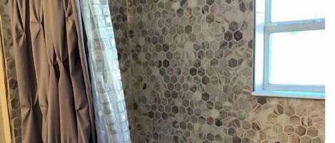 Um banheiro com parede de mosaico de pedra, banheira com estampas florais azuis e uma janela.