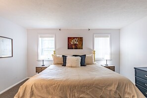 A bedroom with a large bed, two bedside tables, a dresser, and a painting on the wall. - Sunny Home in Private Setting (Rochester)