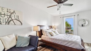 A bedroom with a bed, a sofa, a ceiling fan, and a window with curtains.