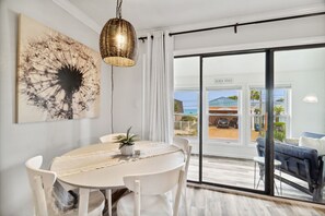 A dining area with a round table, white chairs, a woven pendant light, and a large abstract painting on the wall.