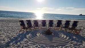 A beach with rows of beach chairs and a fire pit in the sand.