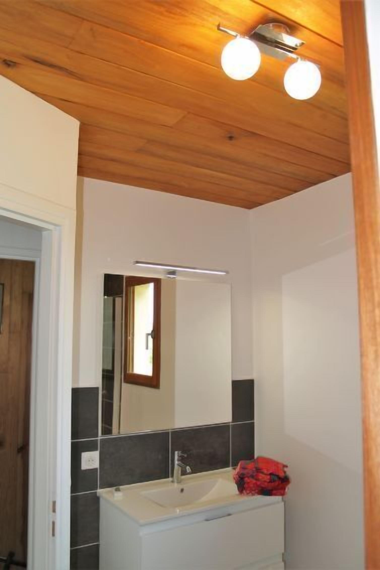 A bathroom with a white sink, dark tiles, a mirror, and a wooden ceiling.