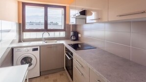 Cocina compacta con lavadora, cafetera y ventana con vistas a edificios.