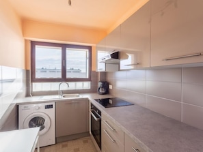 A compact kitchen with a washing machine, a coffee maker, and a window providing a view of buildings. - Le Grand Large by Interhome (Le Lavandou)