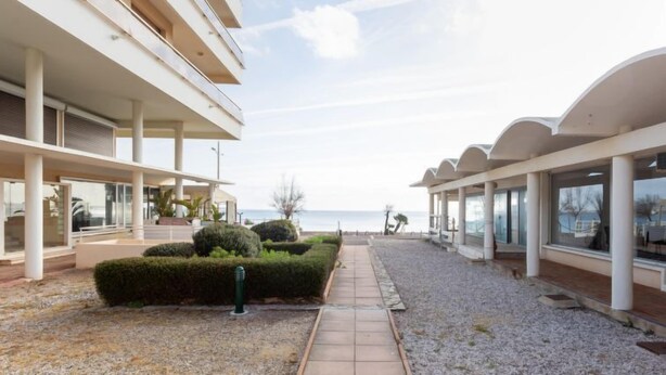 Un edificio moderno con varios pisos, un paseo techado y vista al mar.