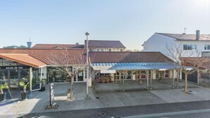 Un bâtiment doté d’une façade en verre et d’un toit en métal, situé à côté d’un bâtiment blanc avec un toit recouvert de tuiles rouges.