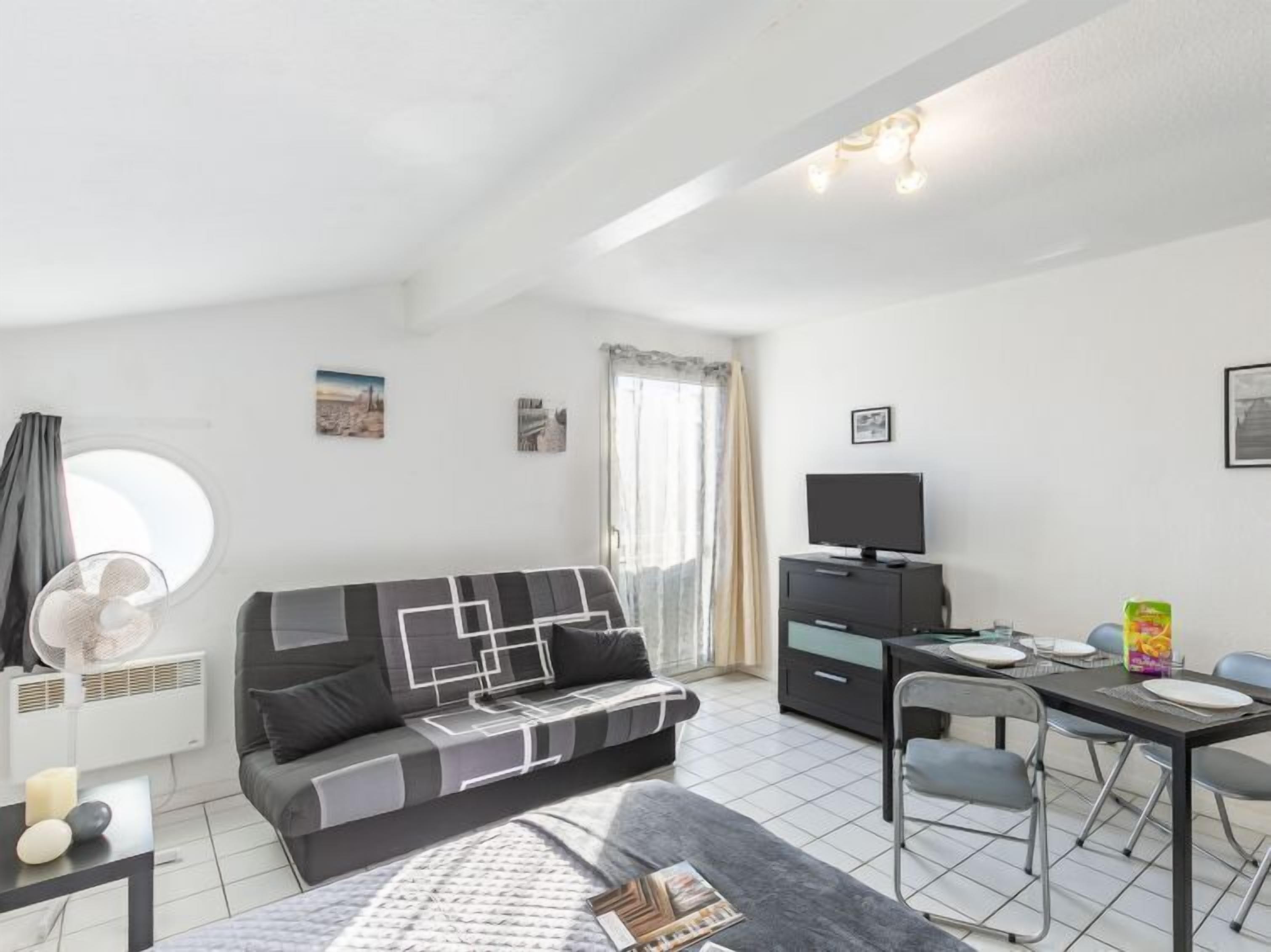 A modern, well-lit room with a sofa, a TV, a dining table with chairs, and a window with curtains.