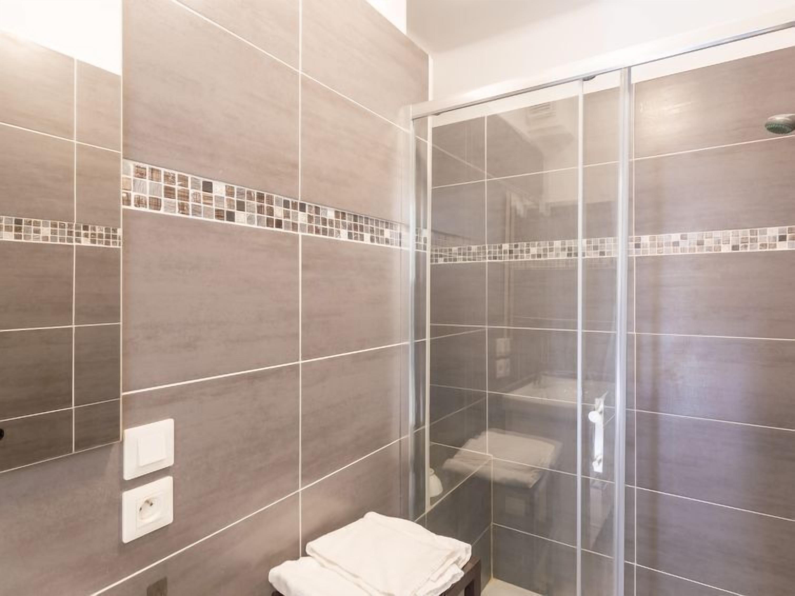 Ein modernes Badezimmer mit einer gläsernen Dusche, gefliesten Wänden und einer kleinen Sitzbank.