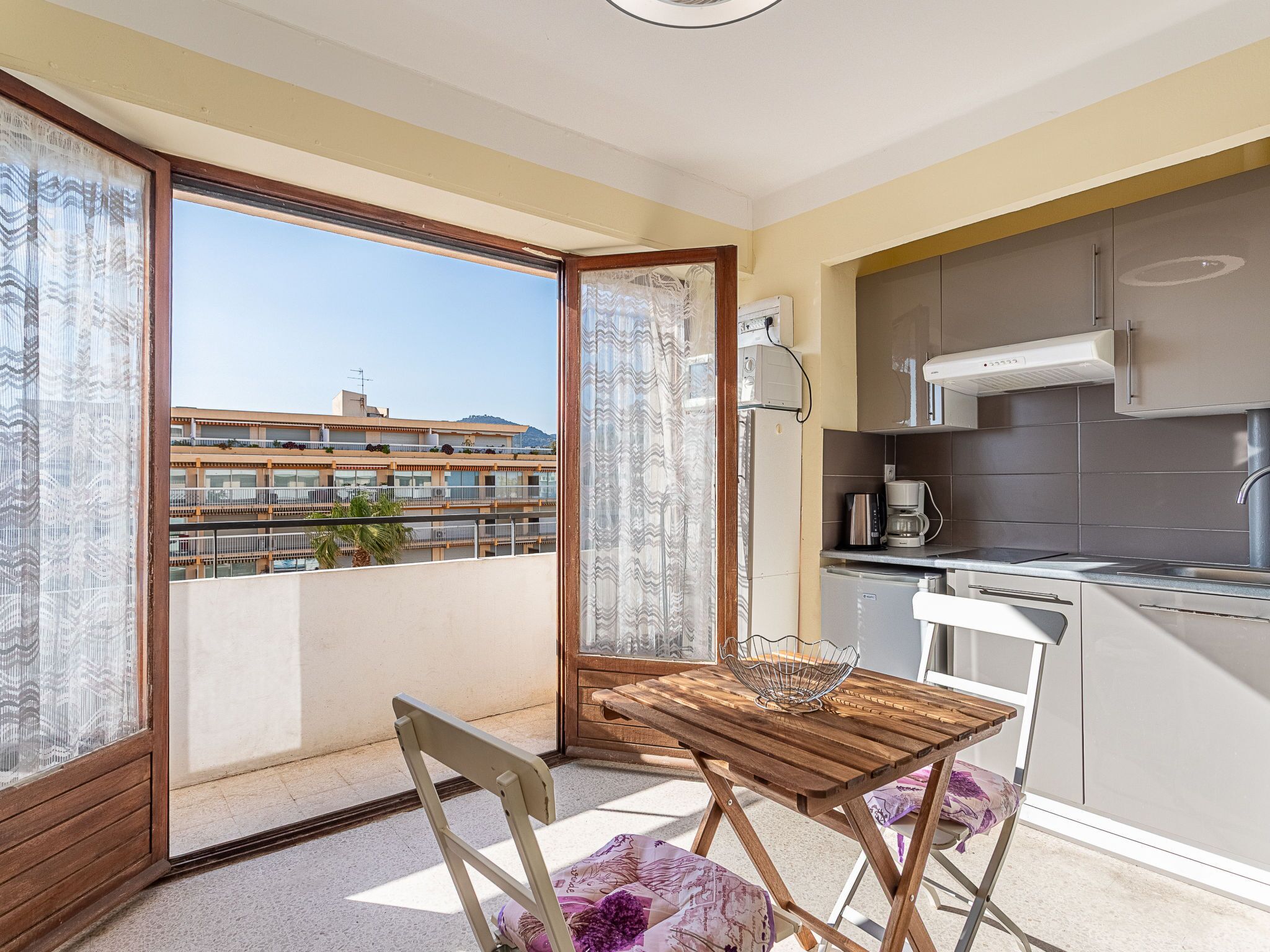 Ein Balkon mit Holztisch und -stühlen, eine Küchenzeile mit modernen Geräten und Blick auf ein gegenüberliegendes Gebäude.