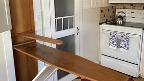 A kitchen with a wooden shelf, a white stove, and a microwave.