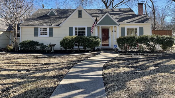 A single-story house with a front porch, a chimney, and a flag.