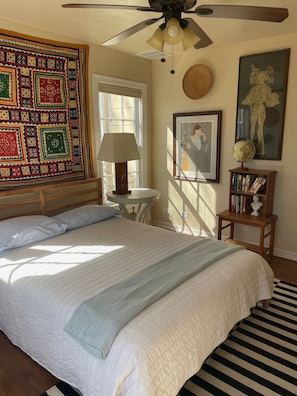 A bedroom with a large bed, a ceiling fan, a quilt, a lamp, a globe, and framed artwork.