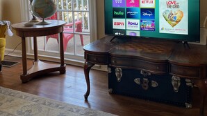 A living room with a television displaying streaming services, a globe on a table, and a view through a large window.