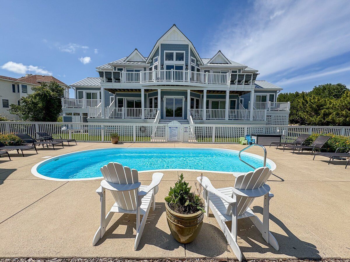 A large house with a swimming pool and white deck chairs.