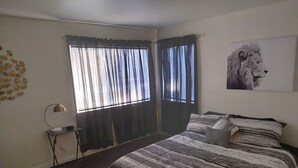 A bedroom with a bed, a desk, a lamp, and a window with curtains.