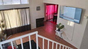 A spacious living area with a fireplace, a dining area with red curtains, and a mounted TV displaying a document.